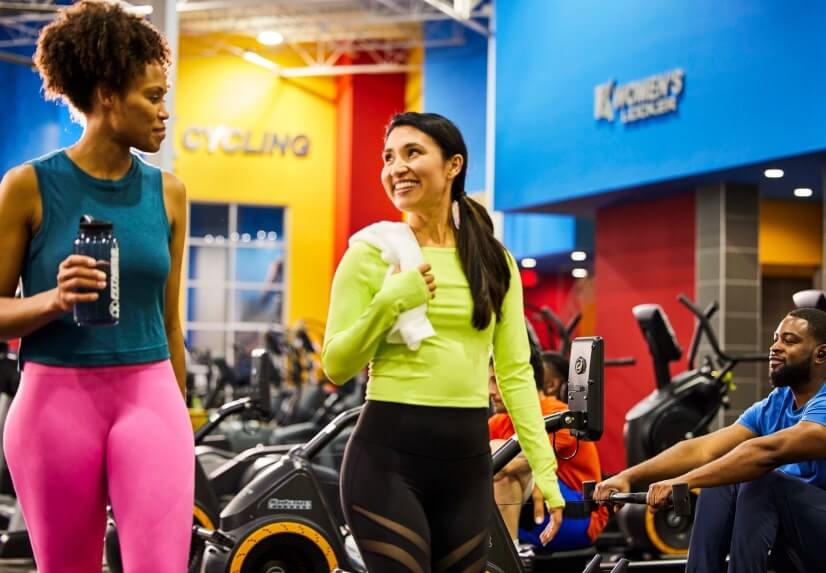 Two women walking along a row of cardio equipment in a fitness connection gym